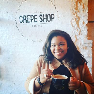 Arlevea Freeman holds a cup of coffee below a sign that says crepe shop