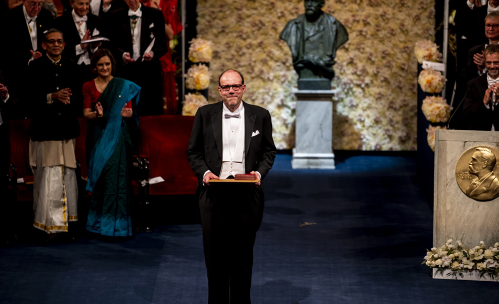 Michael Kremer standing on a stage accepting a nobel prize award.