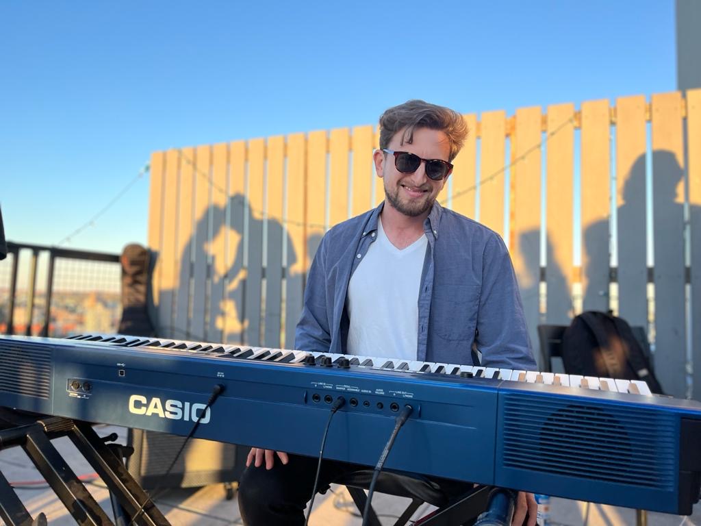 Ross sitting at an electric keyboard outside, smiling