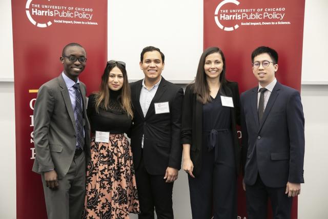 A group photo of five Obama Scholars/MAIDP'19 in formal clothes, in front of banners with the Harris Public Policy logo