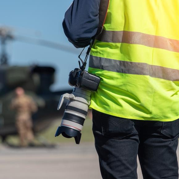 A military photographer, a reporter, in a signal yellow vest, ready to work in front of a military helicopter.